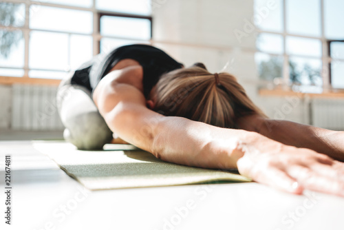 Young athletickwoman doing yoga exercise on fitness mat in white sunny gym early morling. Sporty girl rests after a stressful workout photo