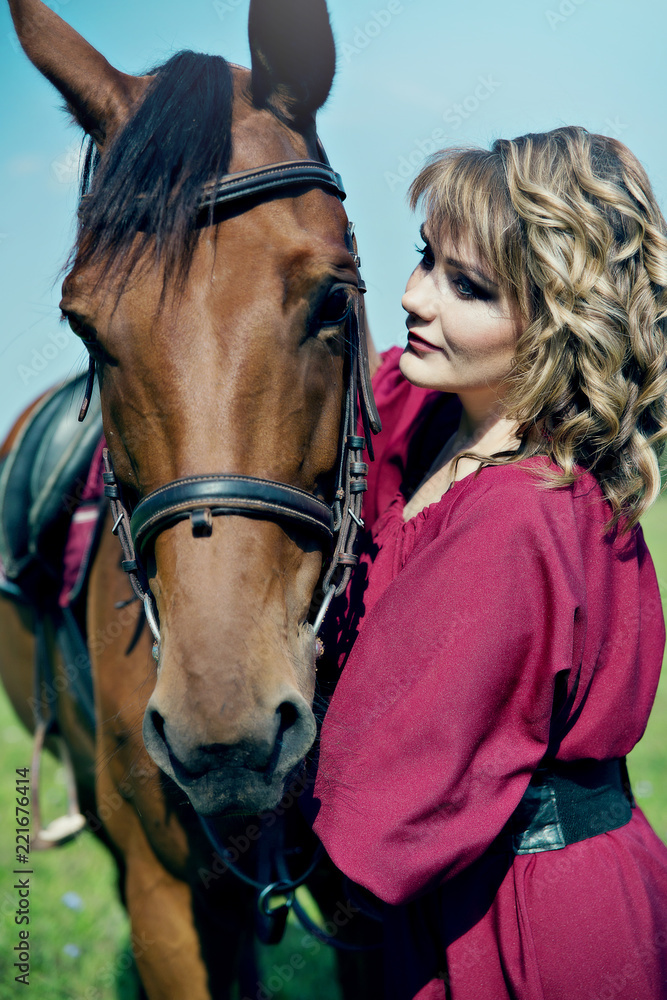 Obraz premium Beautiful girl in a red dress stands next to the brown horse.
