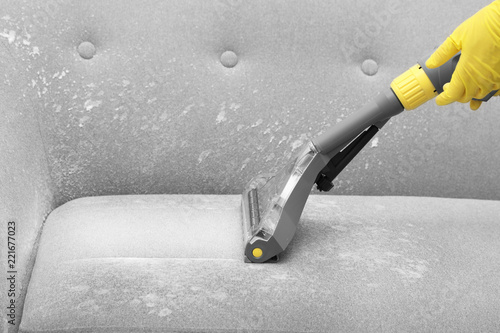 Janitor removing dirt from sofa with upholstery cleaner, closeup