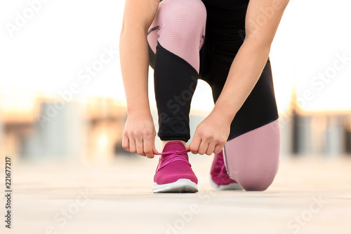 Young woman tying shoelaces before running outdoors, focus on legs