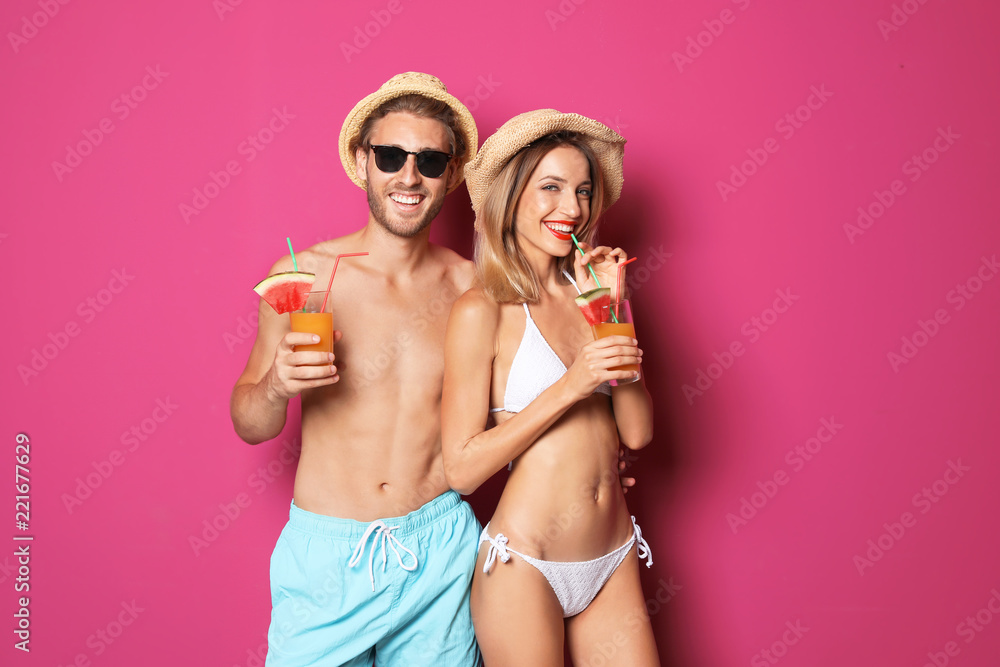 Fototapeta premium Happy young couple in beachwear with cocktails on color background