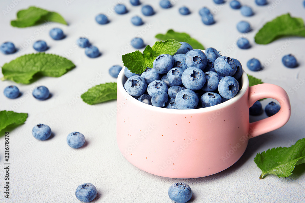 Cup with juicy blueberries and green leaves on color table Cup with juicy blueberries and green leaves on color table