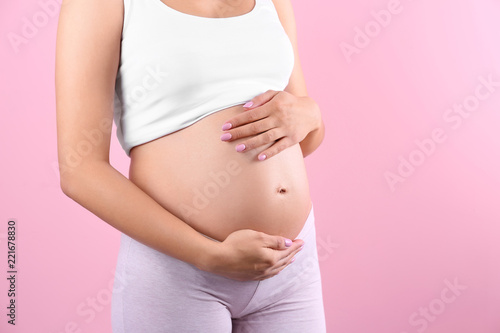 Young pregnant woman holding hands on belly against color background, closeup. Space for text