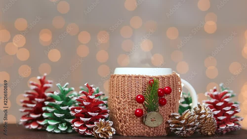 Closeup front view of one cup with hot drink on brown wooden table at holiday shiny lights background. White mug decorated with Christmas traditional elements. Real time full hd video footage. Closeup front view of one cup with hot drink on brown wooden table at holiday shiny lights background. White mug decorated with Christmas traditional elements. Real time full hd video footage.
