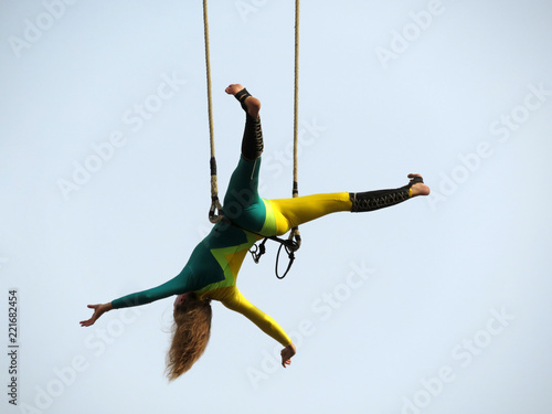 Foto Girl aerial gymnast hanging upside down on trapeze isolated on sky background