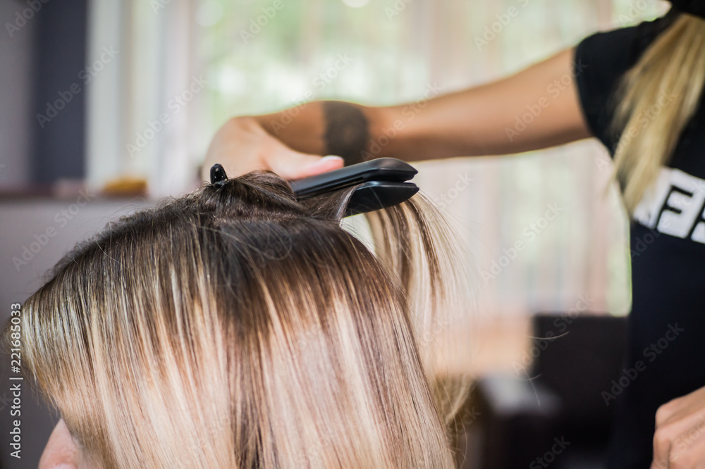 Naklejka premium The hairdresser pulls the client hair, after washing his head, applying nutrients to the hair and drying the hair with a hair dryer, botox hair, restoring and nourishing the hair