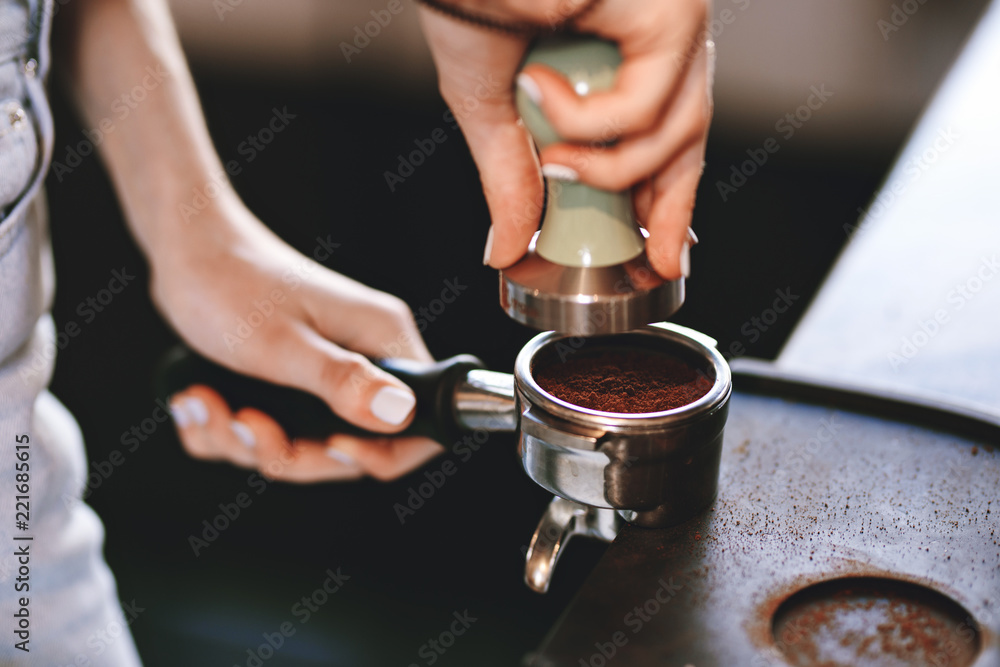 A young pretty slim girl,wearing casual outfit,is cooking coffee in a modern coffee shop. It focuses on the process.