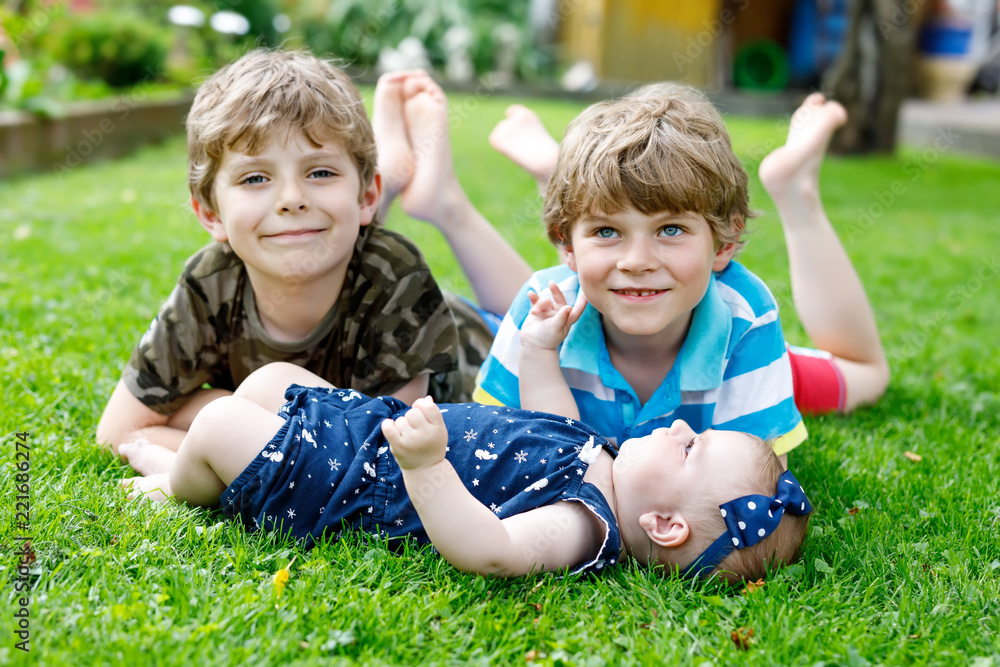 Two little happy kid boys with newborn baby girl, cute sister. Siblings on grass in summer or spring in garden. Kids bonding. Family of three children. Two little happy kid boys with newborn baby girl, cute sister. Siblings on grass in summer or spring in garden. Kids bonding. Family of three children.