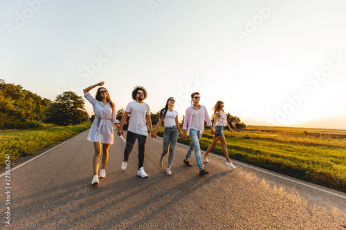 Company of happy young stylish guys walk on a country road on a sunny day