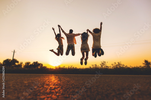 Company of young girls and guys are jumping in the field on a summer day and holding their hands up at sunset photo