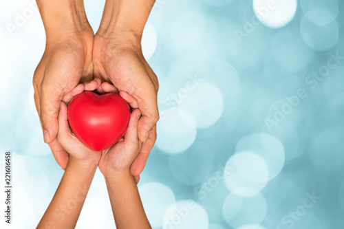 Hands of male dad and little child girl holding red heart ball together with blur green natural light bokeh background. Happy father's day father and daughter concept.
