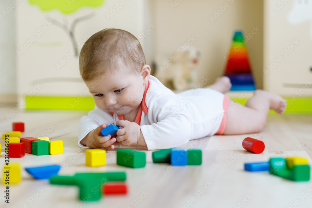 Cute happy smiling baby playing with colorful rattle toys. New born child, little girl learning crawling. Family, new life, childhood, beginning concept. Baby learning grab wooden blocks. Cute happy smiling baby playing with colorful rattle toys. New born child, little girl learning crawling. Family, new life, childhood, beginning concept. Baby learning grab wooden blocks.