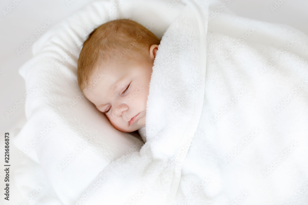 Cute adorable newborn baby wrapped in white blanket, sleeping in kids bed or cocoon. Closeup of peaceful child, little baby girl sleeping. Swaddling as method for calm down child. Cute adorable newborn baby wrapped in white blanket, sleeping in kids bed or cocoon. Closeup of peaceful child, little baby girl sleeping. Swaddling as method for calm down child.