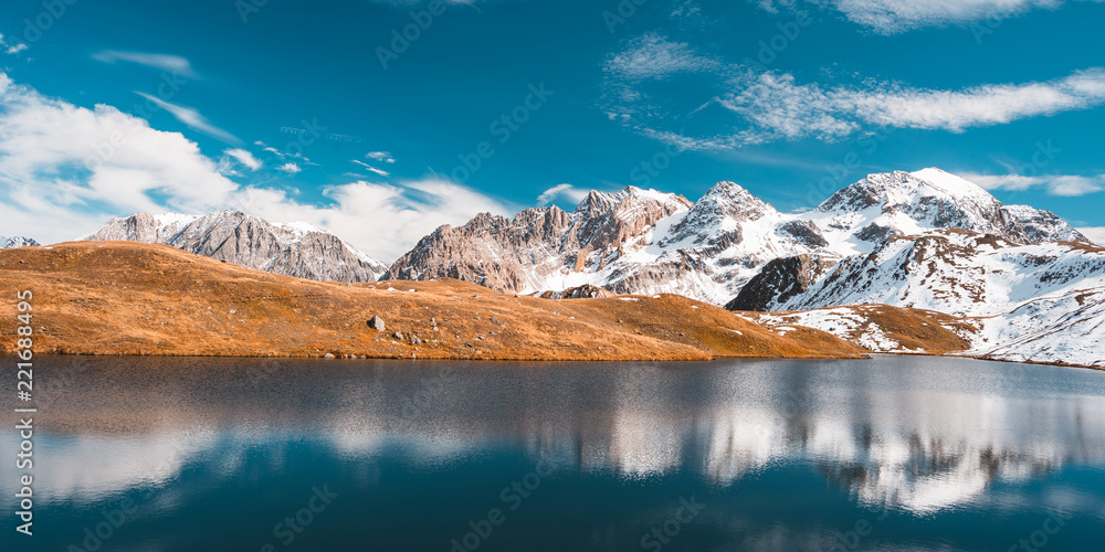 Fototapeta premium Colorful sunlight behind majestic mountain peaks of the Italian - French Alps, viewed from distant. Fog and mist covering the valleys below, autumnal landscape, cold feeling.
