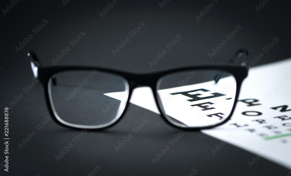 Glasses on eye test letter chart on optician table. Ophthalmology or optometry clinic. Focus through lens. Eyesight exam. Glasses on eye test letter chart on optician table. Ophthalmology or optometry clinic. Focus through lens. Eyesight exam.