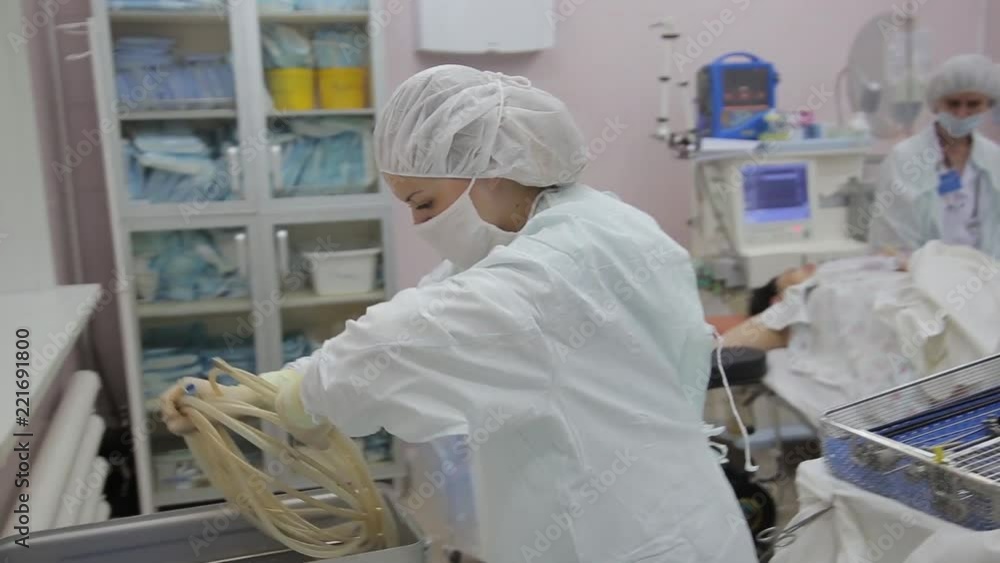 A female surgeon assistant moves the surgical instruments into a container A female surgeon assistant moves the surgical instruments into a container
