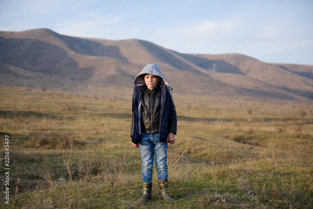 cute little boy in jacket and jeans and hood in mountains in autumn