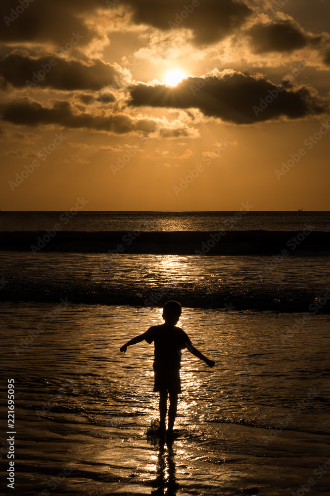 A single child playing in the ocean at sunset