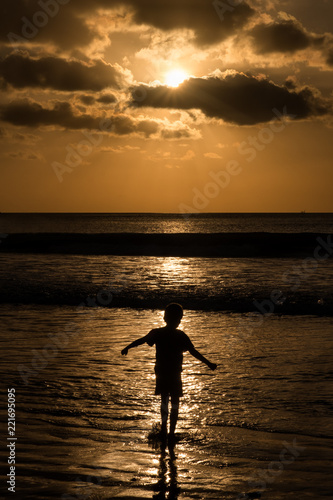 A single child playing in the ocean at sunset