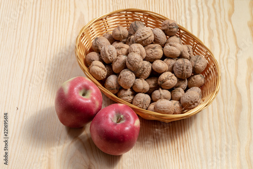 Two red apples beside a basket full of walnuts