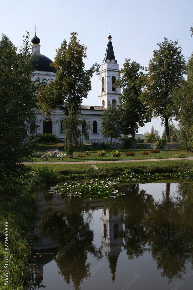 The white Orthodox Church in the park is reflected in a pond with lilies