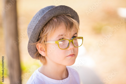 The portrait of blonde boy in the hat and green glasses