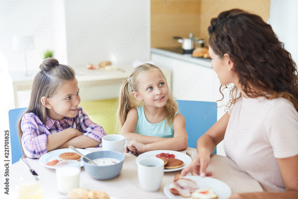 Cute daughters talking to their mom by breakfast while having homemade food