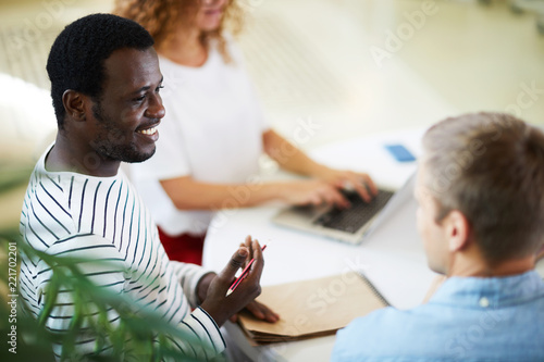 African-american guy consulting with one of his groupmates while preparing home assignment
