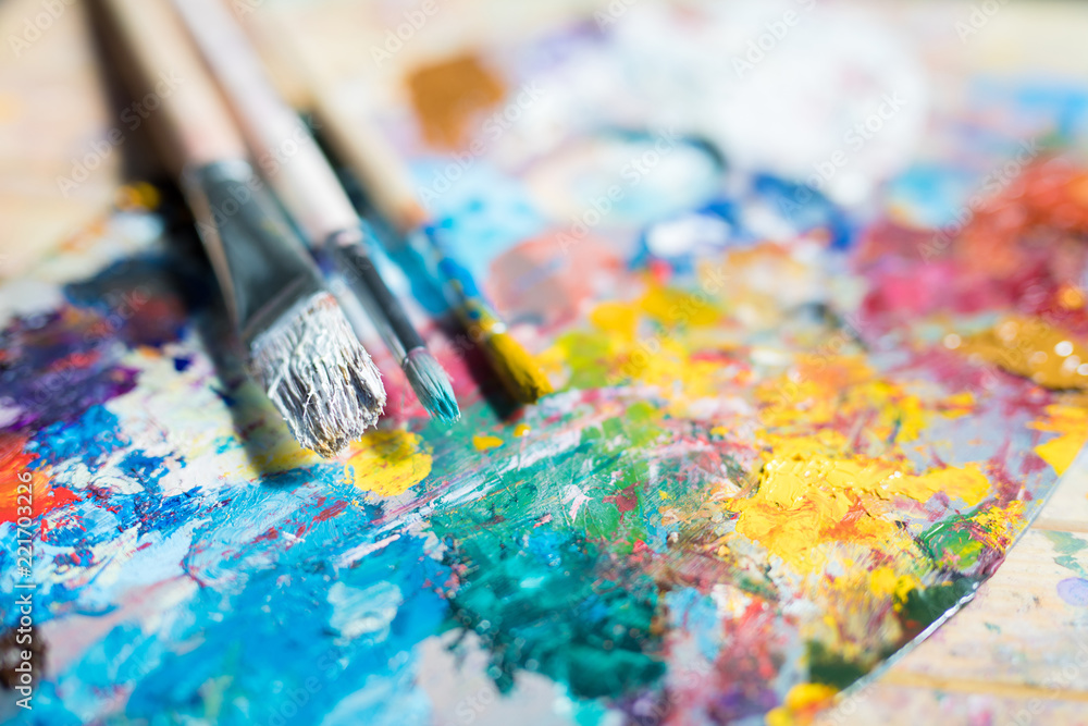 Bunch of paintbrushes in paints over palette with mixed colors such as yellow, blue and others