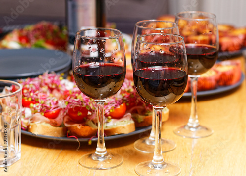 House party: four glasses of red wine, fresh sandwiches and sweets on a wooden table