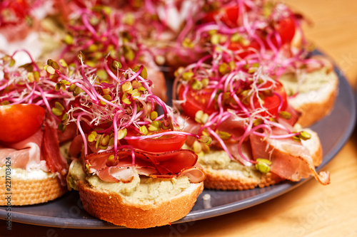 Small fresh homemade sandwiches with bread, avocado paste, sprouts, Parma ham and coctail tomato prepared to house party