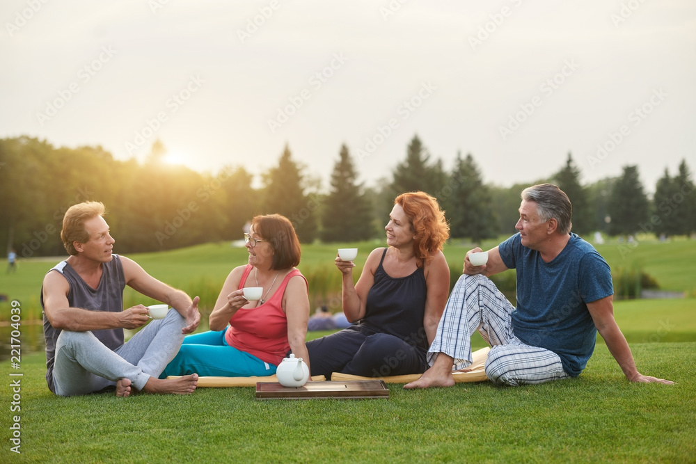 Mature man telling a story to his friends. Four happy people drinking tea in the summer park. Mature man telling a story to his friends. Four happy people drinking tea in the summer park.
