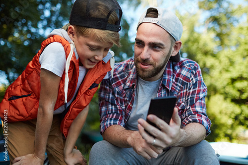 Young man with smartphone showing his son curious video about fishing or some other lesiure pastime photo