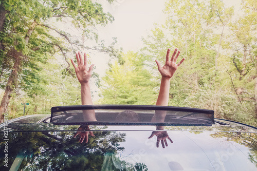Boy putting his  hands out of the car sunroof top, driving down a country road photo