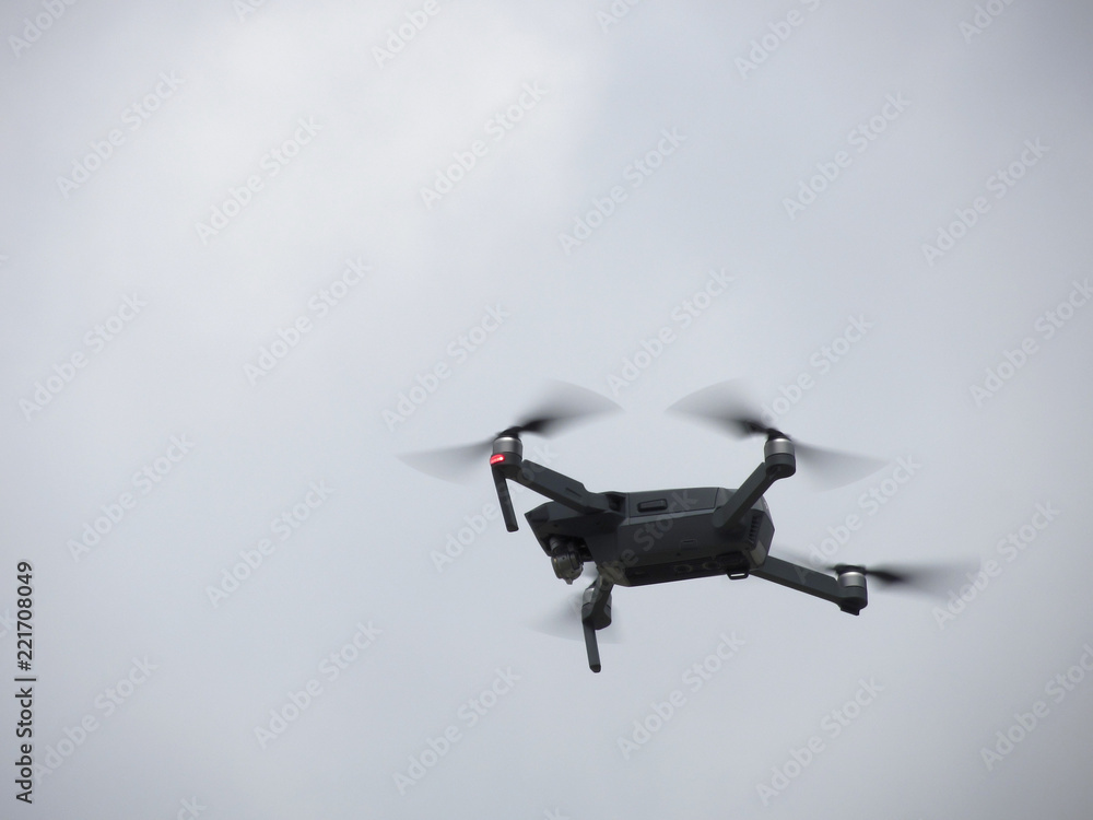 Quadcopter drone flying overhead in cloudy sky Quadcopter drone flying overhead in cloudy sky
