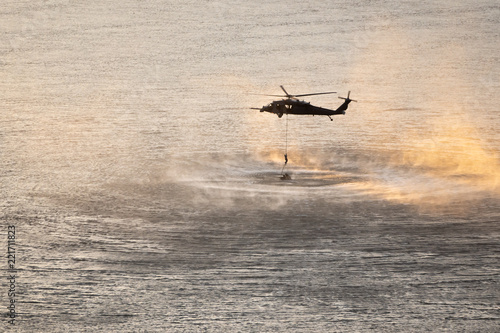 Helicopter in plumes of water vapor and drizzle at sunset. Mock up rescue mission above the Columbia river. Navy person descends down the rope.