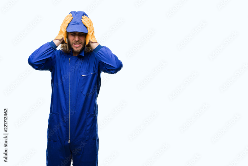 Young handsome mechanic man with long hair over isolated background suffering from headache desperate and stressed because pain and migraine. Hands on head. Young handsome mechanic man with long hair over isolated background suffering from headache desperate and stressed because pain and migraine. Hands on head.