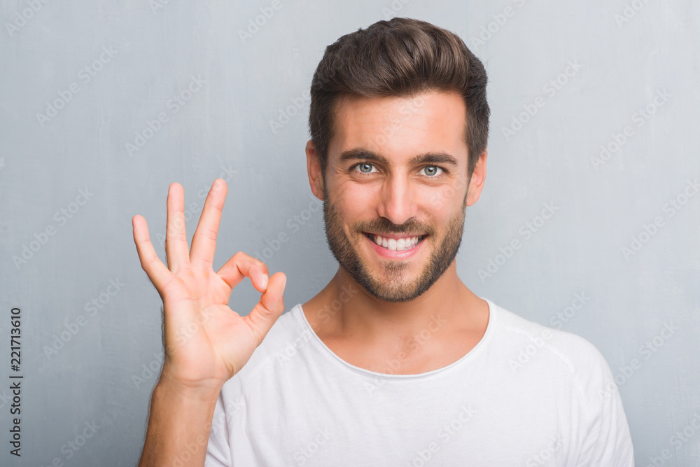 Handsome young man over grey grunge wall doing ok sign with fingers, excellent symbol Handsome young man over grey grunge wall doing ok sign with fingers, excellent symbol