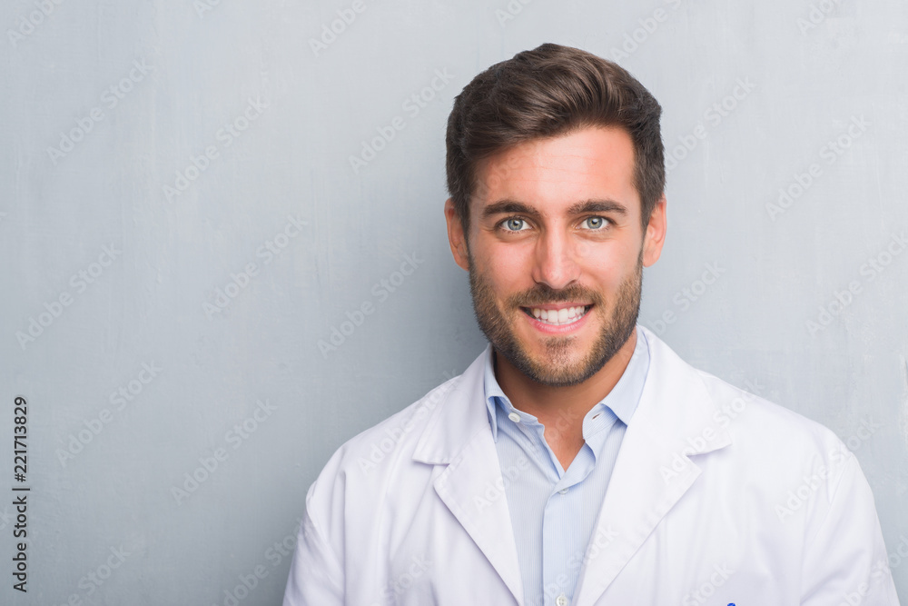 Handsome young professional man over grey grunge wall wearing white coat with a happy and cool smile on face. Lucky person. Handsome young professional man over grey grunge wall wearing white coat with a happy and cool smile on face. Lucky person.