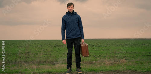 man with a suitcase in his hands is looking in the field.