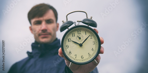 businessman with an alarm clock in his hands against the sky.