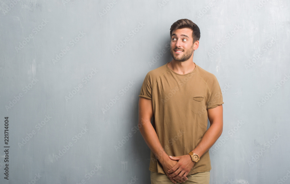 Handsome young man over grey grunge wall smiling looking side and staring away thinking.