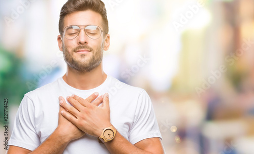 Young handsome man wearing glasses over isolated background smiling with hands on chest with closed eyes and grateful gesture on face. Health concept. photo