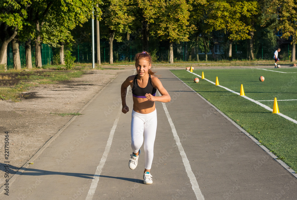 A teenage girl is running on a treadmill at the school stadium.