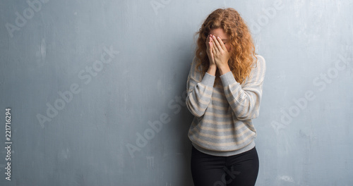 Young redhead woman over grey grunge wall with sad expression covering face with hands while crying. Depression concept.