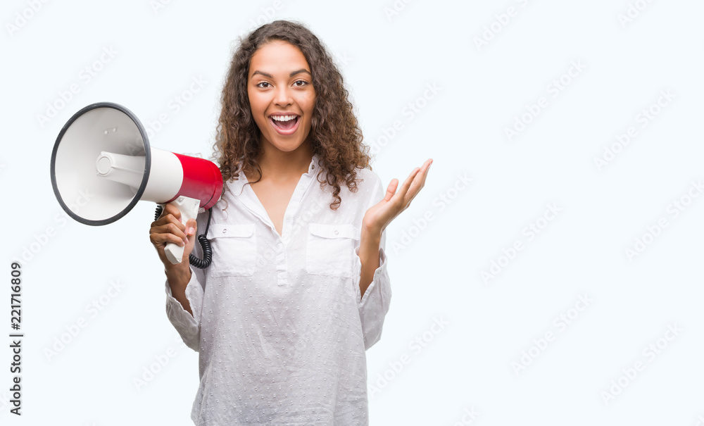 Young hispanic woman holding megaphone very happy and excited, winner expression celebrating victory screaming with big smile and raised hands Young hispanic woman holding megaphone very happy and excited, winner expression celebrating victory screaming with big smile and raised hands