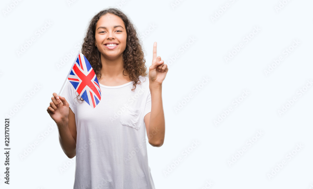 Young hispanic woman holding flag of United Kingdom surprised with an idea or question pointing finger with happy face, number one Young hispanic woman holding flag of United Kingdom surprised with an idea or question pointing finger with happy face, number one