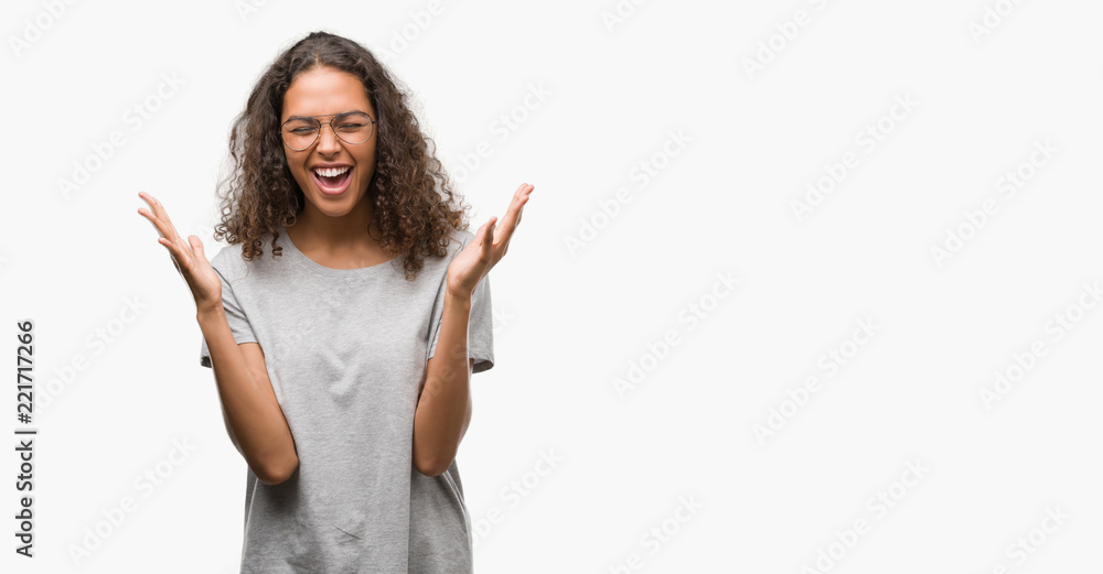 Beautiful young hispanic woman wearing glasses celebrating mad and crazy for success with arms raised and closed eyes screaming excited. Winner concept Beautiful young hispanic woman wearing glasses celebrating mad and crazy for success with arms raised and closed eyes screaming excited. Winner concept