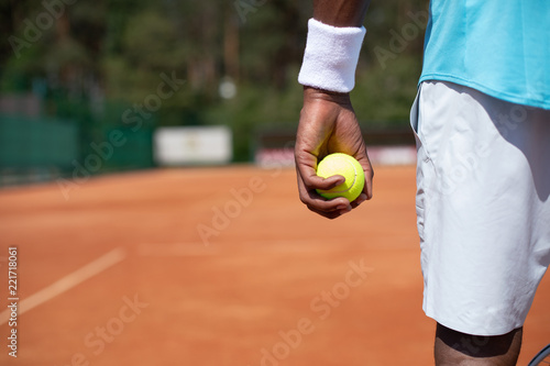 Close-up of male hand with sport outfit. Guy is standing on sunny court and playing active game. Copy space in left side