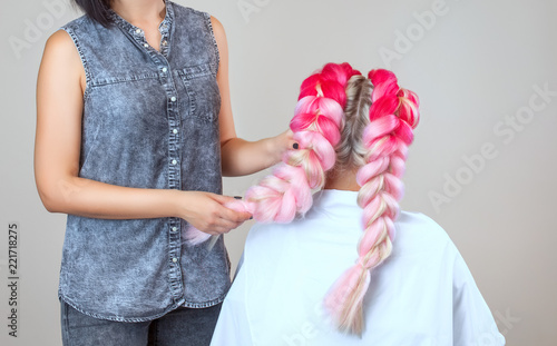 The hairdresser weaves braids with pink kanekalons beautiful blonde beauty salon. photo